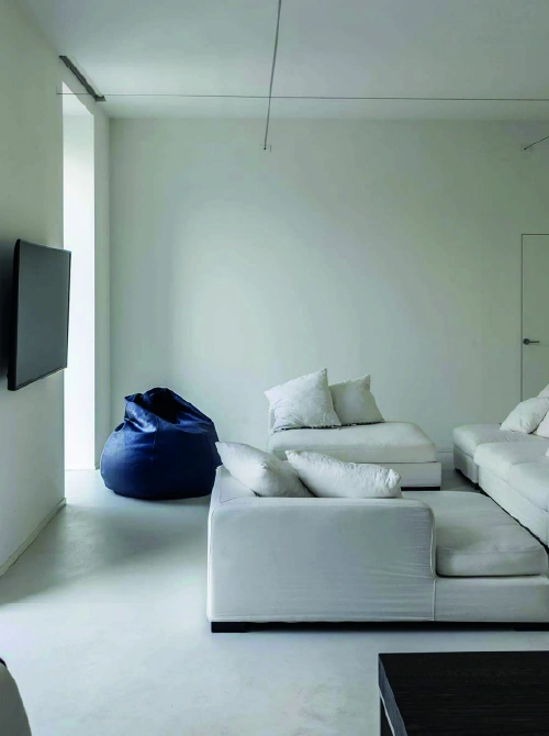 Soggiorno minimal luminoso con divano bianco e pouf blu